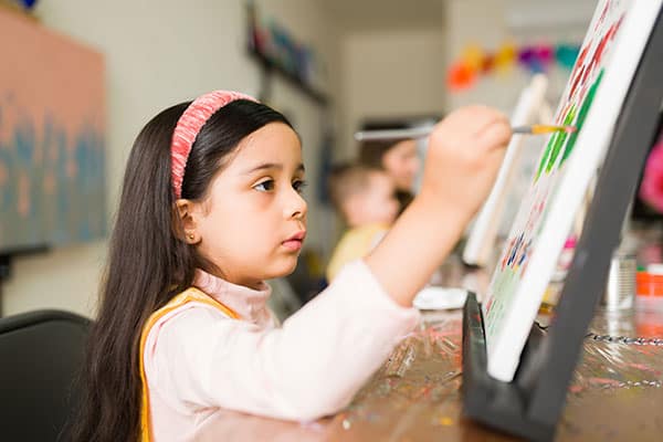 hispanic elementary girl with focused expression while painting